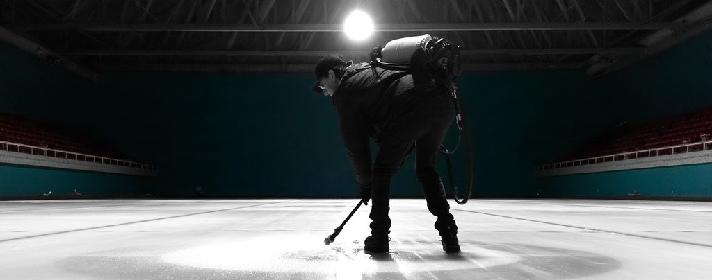 Ice technician alone on a dark sheet pebbling the ice under a single overhead light